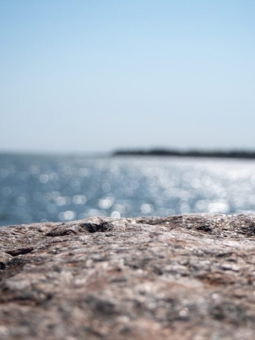 a bottle of beer sitting on top of a rock next to the ocean